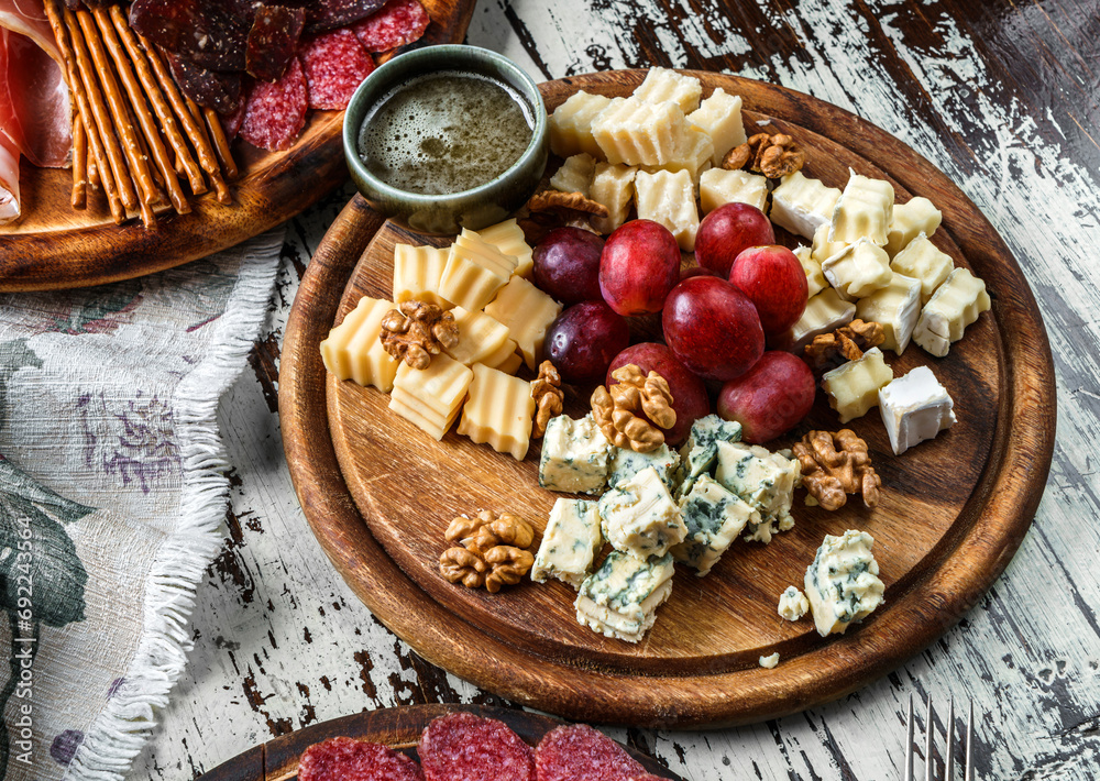 Cheese plate with parmesan, maasdam, blue cheese, brie cheese, cheddar with fruits and nuts on board over wooden background with glass of wine. Snacks and Wine appetizers set, top view