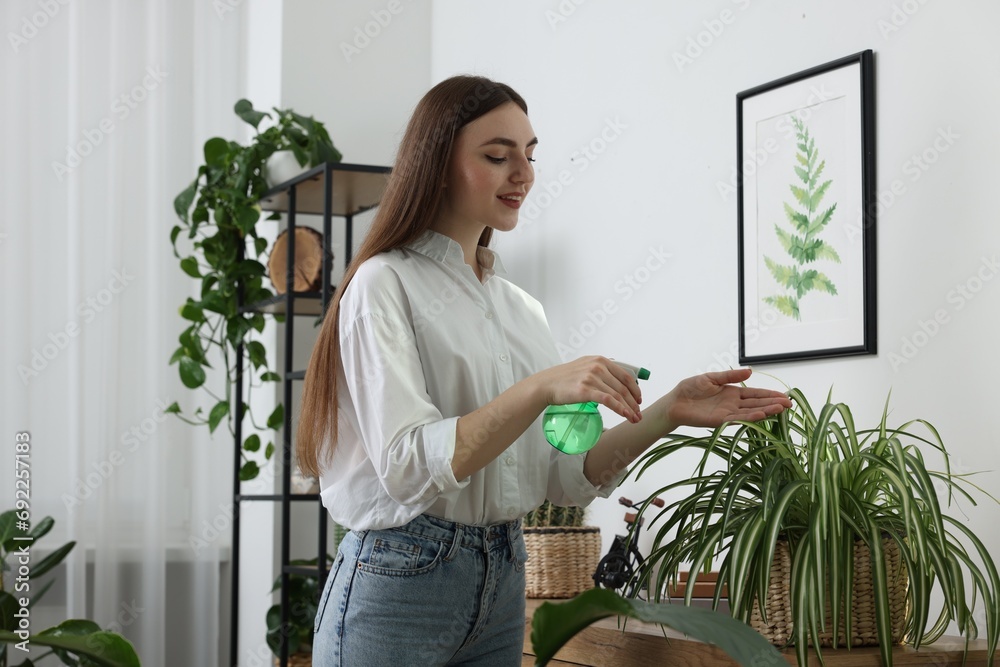 Beautiful young woman spraying green houseplants at home