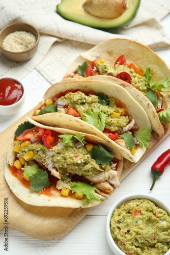 Delicious tacos with guacamole, meat and vegetables on white wooden table