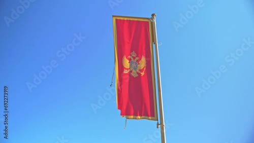 Flag of Montenegro flutters in wind against blue sky. Sun throws rays on flag of Montenegro. Montenegrins hung flag to show love for state photo