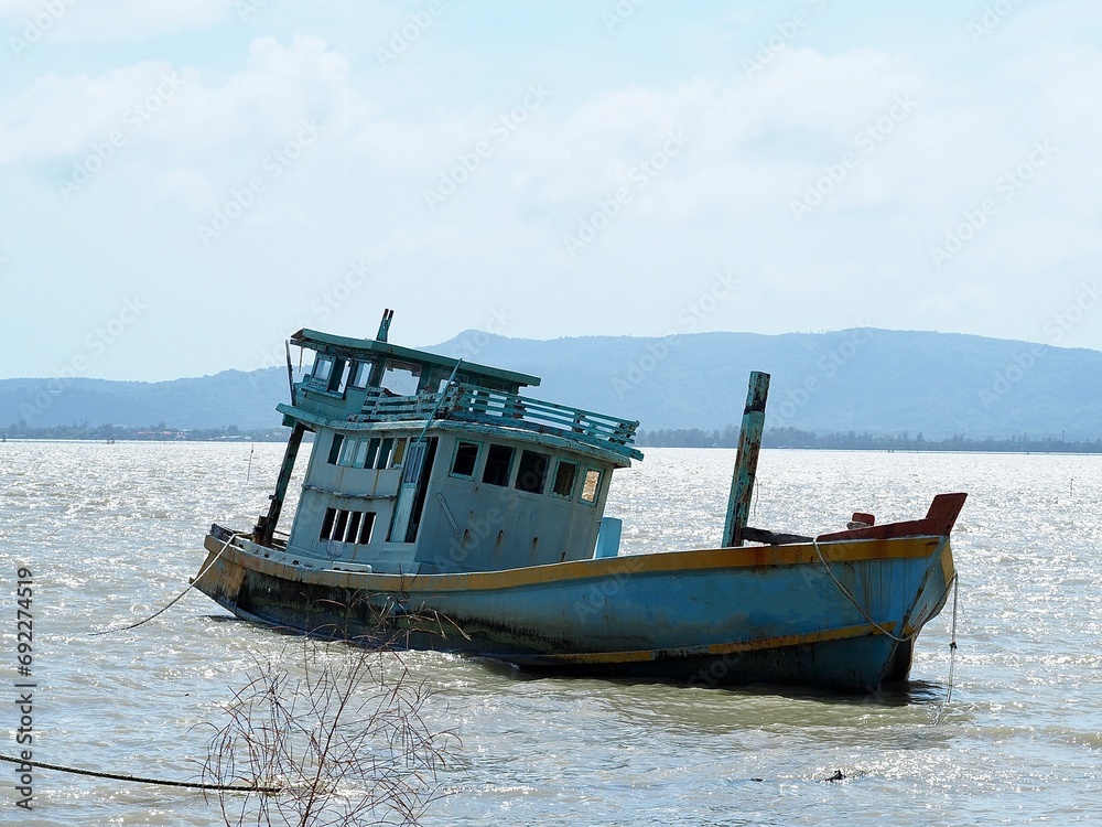 A photograph of a dilapidated fishing boat wreck, reaching the end of its service life, abandoned by the fishermen on the shoreline