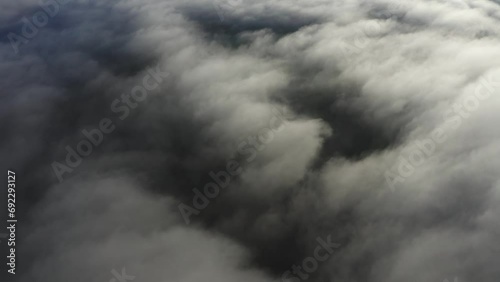 Flying over bright white clouds and dark mysterious land in shadow below photo