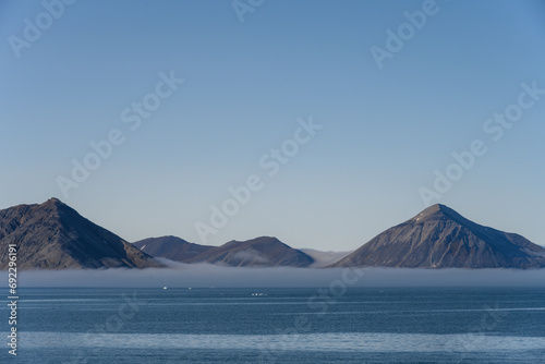 Scenic mountain range rising up out of the Arctic ocean and early morning fog at Gnalodden, Svalbard, peaceful polar nature background 