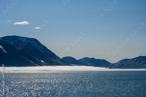 Peaceful early morning pastel blue landscape of mountain range, fog, sky, and Arctic ocean, Svalbard, as a polar nature background 