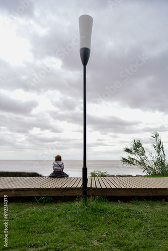 A woman sitting on her back, looking towards the river, on the coastal road in Vicente Lopez, Buenos Aires, Argentina photo