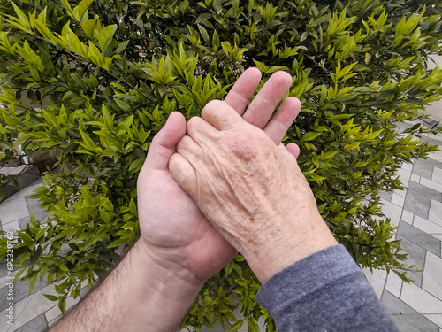 Man supporting and motivating an elderly woman, while holding her hands in a nature background.