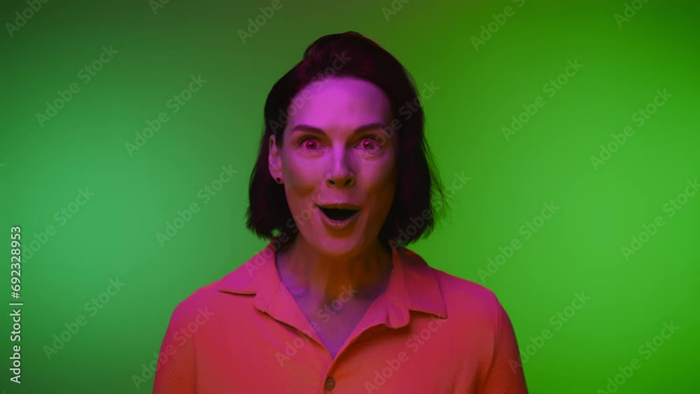 Surprising Portrait of Happy Adult Woman with Open Mouth Looking at Camera Closeup. Emotions of One Modern Lady Standing on Neon Colour Shot. Front of Mature Head in Bright Light of Cool Illumination Surprising Portrait of Happy Adult Woman with Open Mouth Looking at Camera Closeup. Emotions of One Modern Lady Standing on Neon Colour Shot. Front of Mature Head in Bright Light of Cool Illumination