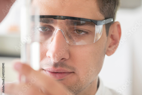 scientist male with lab glasses and gloves watching to green liquid