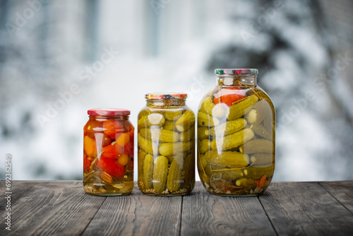 Canned vegetables: tomatoes, cucumbers, peppers on a wooden rustic table against the background of a winter window.