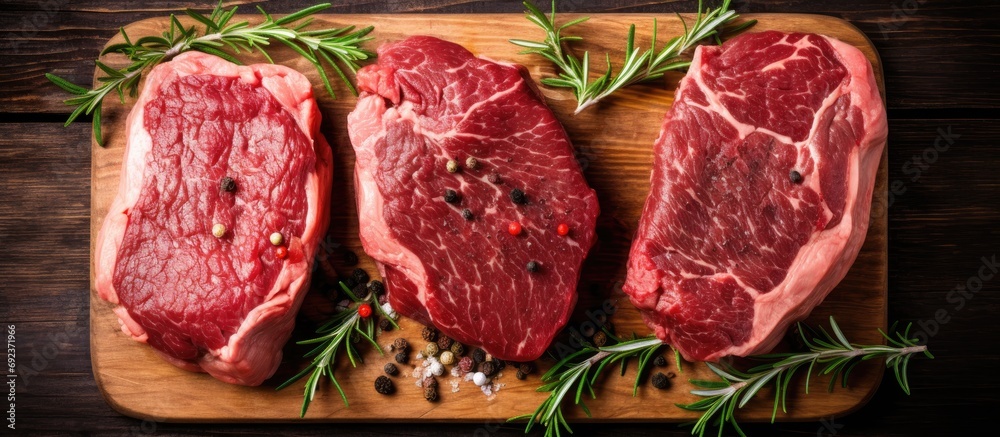 Three raw ribeye beef steaks, on a wooden butcher block, seen from above.