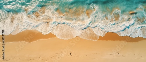 Aerial view of the foamy waves touching the sandy beach, with the serene blue ocean in the background.