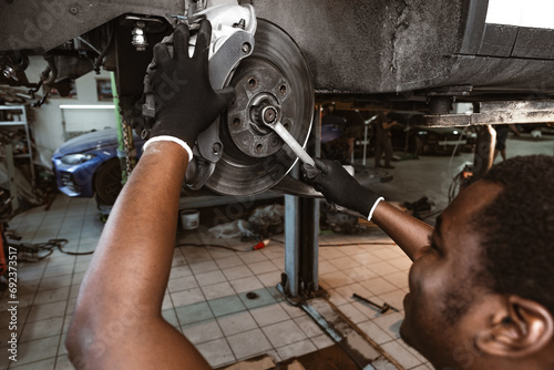African male auto-mechanic repairing car brakes under the car in auto service