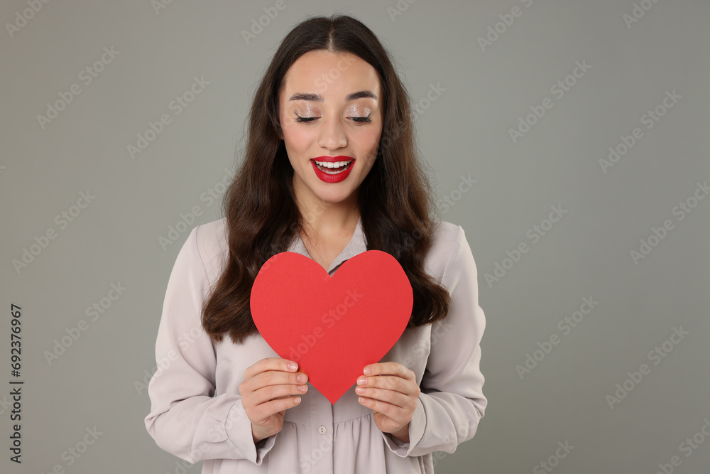 Beautiful young woman with paper heart on grey background Beautiful young woman with paper heart on grey background