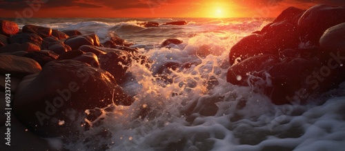As the sun sets, casting a red hue on the landscape, the mesmerizing waves of the sea splash against the stones, creating a beautiful texture and background of nature. The sound of raindrops hitting