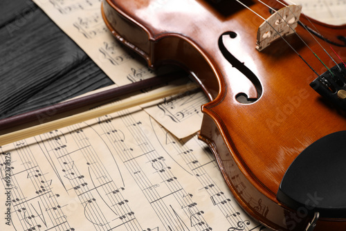 Violin, bow and music sheets on black wooden table, closeup photo