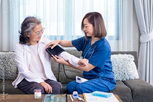 Senior woman got medical service visit from caregiver nurse at home while having blood pressure test using sphygmomanometer on for health care and pension welfare insurance
