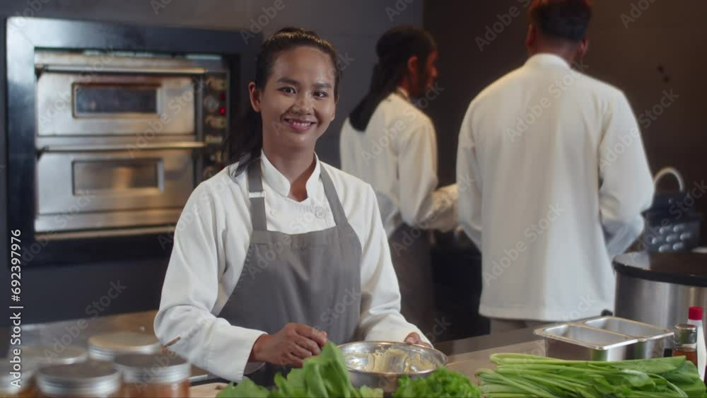 Medium portrait of cheerful female Asian sauce chef cooking at restaurant kitchen and looking at camera Medium portrait of cheerful female Asian sauce chef cooking at restaurant kitchen and looking at camera