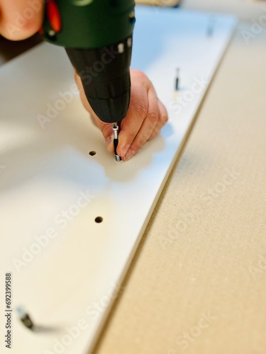 Close-up of a man's hands using an electric screwdriver to assemble a piece of furniture photo