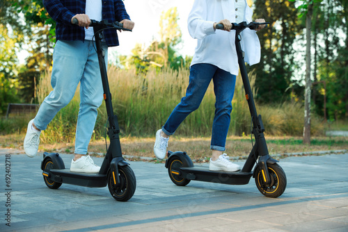 Couple riding modern electric kick scooters in park, closeup