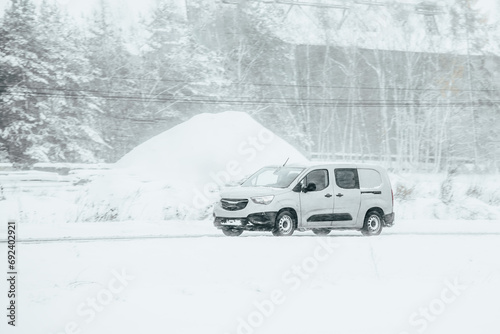 Van driving in the snow. Logistics on a snowy winter day. Delay of cargo delivery due to snowfall in winter. Side view of a commercial cargo van.