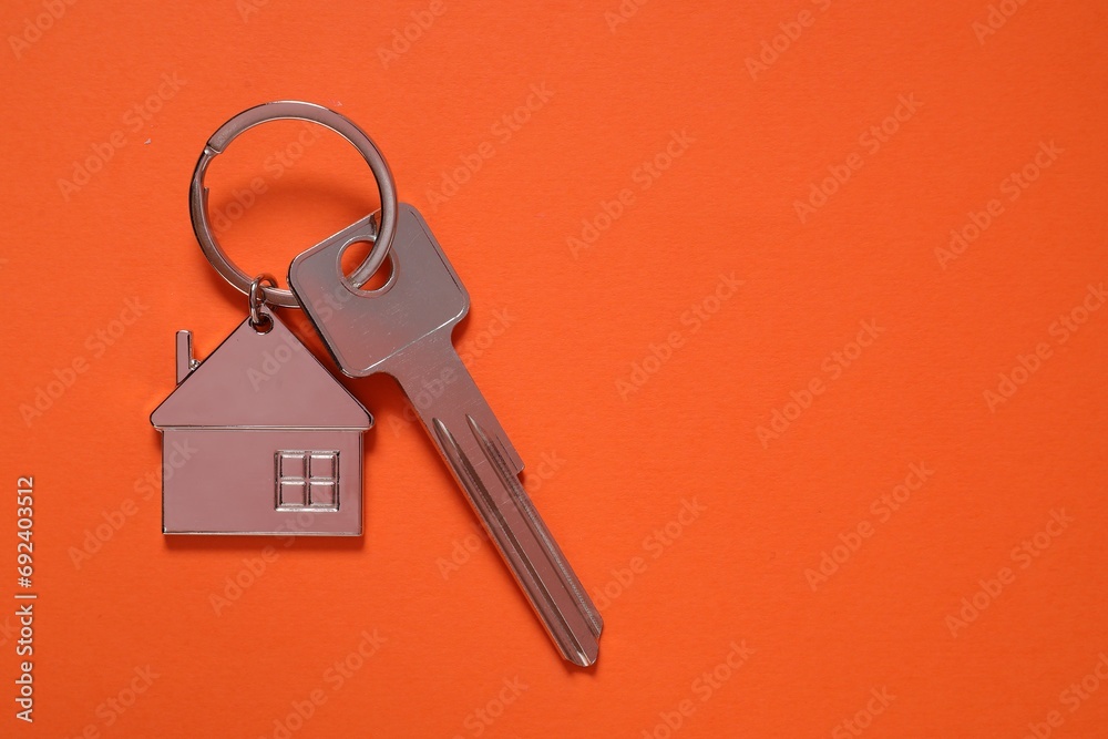 Metallic key with keychain in shape of house on orange background, top view. Space for text Metallic key with keychain in shape of house on orange background, top view. Space for text