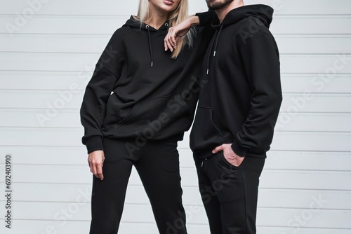 Man and woman wear black hoodies.  A fashion template for print and branding on hoodie. trendy couple on the street wearing casual apparel with no face visible. No logo sweater and pullover with hood. photo