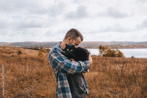 A Loving Man and His Black Cat in the Autumn Forest. He Carries His Pet on His Shoulder and Walks with a Leash in the Park. © AlexGo