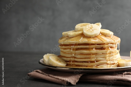 Tasty pancakes with sliced banana and honey on gray table, space for text