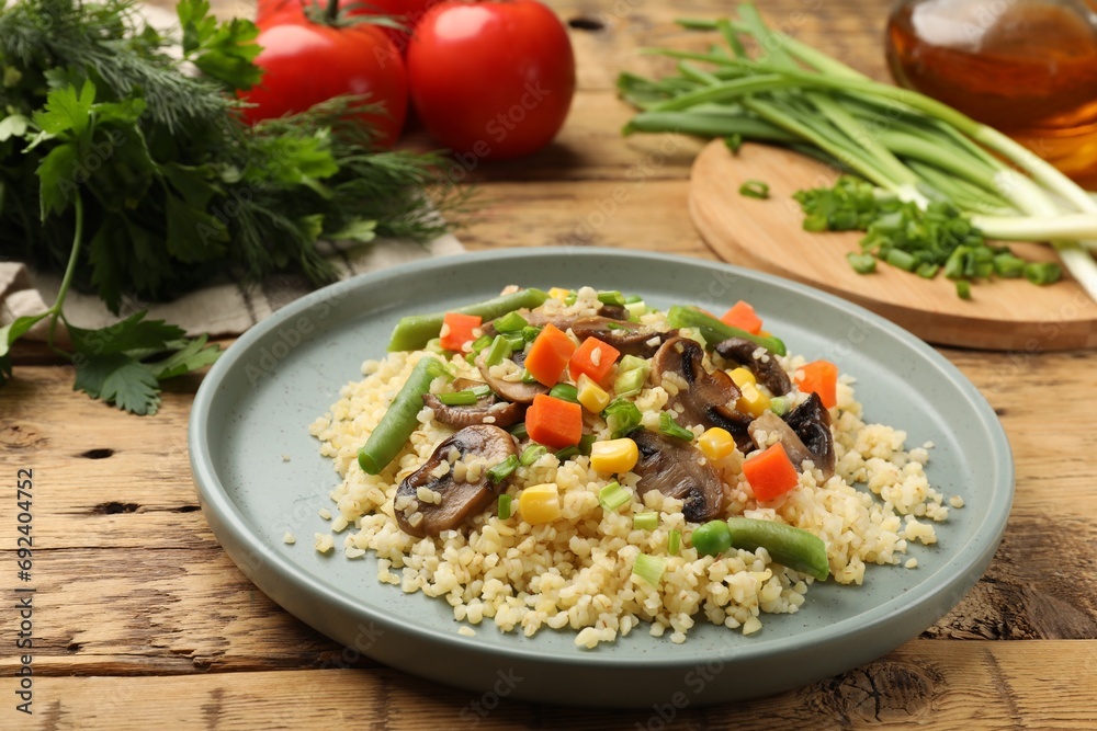Delicious bulgur with vegetables and mushrooms on wooden table, closeup Delicious bulgur with vegetables and mushrooms on wooden table, closeup