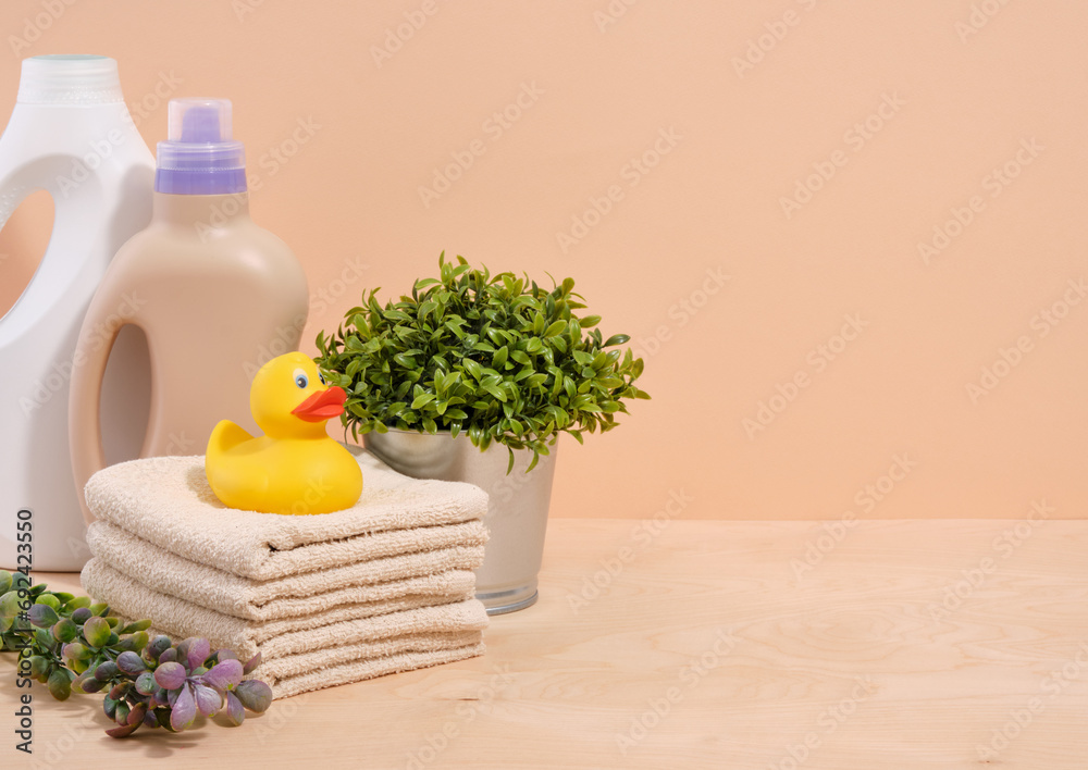 Cleanliness and household. Copy space for text. Yellow rubber duck sits on the clean fresh towels. Washing powders and a green plant in a metal pot.