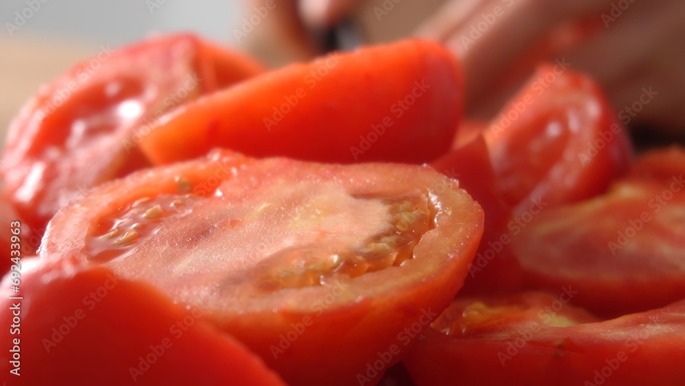Close-Up shot of Juicy Tomato Slices and Halves. In the blurry background, a girl is cutting tomatoes.