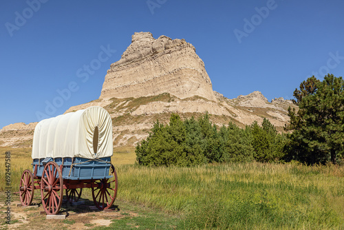 Wagon on display along the Oregon Trail at the entrance of the Mitchell Pass in the vicinity of Sotts Bluff National Monument with Eagle Rock on the right photo