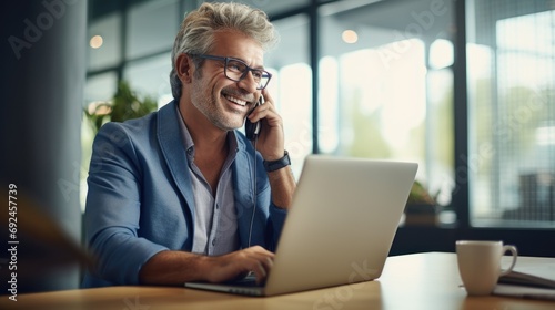 Happy busy older mid aged business man professional expert or entrepreneur making phone call speaking with client communicating on cellphone using laptop computer sitting at desk in office. Copy space photo