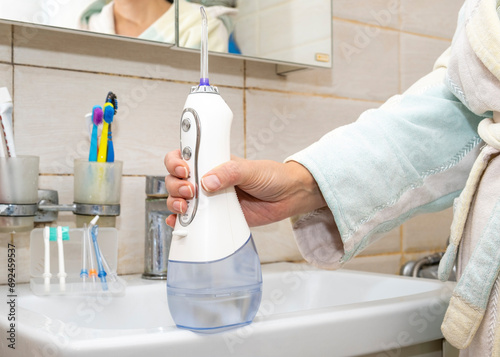 A woman's hand holds an individual irrigator in her hand against the background of the bathroom. Brushing teeth concept. photo