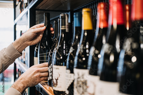 Customer Selecting Wine Bottle from Store Shelf. A person's hand picking a wine bottle from a diverse selection on a well-stocked wine shop shelf photo