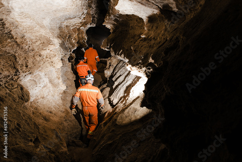 Three men, strong physique, explore the cave. Men dressed in special clothes to pass through the cave and stopped, looking at the map photo