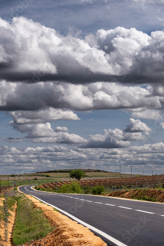 A picturesque view of a road winding through Ribera del Duero's spring vineyards under a clear sky adorned with scattered clouds