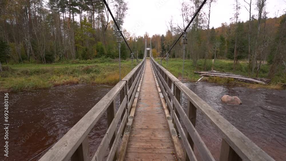 A sturdy wooden suspension bridge spans across a calm river, surrounded by the vibrant greenery of a forest. A sturdy wooden suspension bridge spans across a calm river, surrounded by the vibrant greenery of a forest.