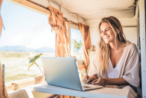 Independent woman sitting inside a camper van in using a laptop. Living and working inside camper van vehicle in travel and digital nomad free lifestyle.  photo