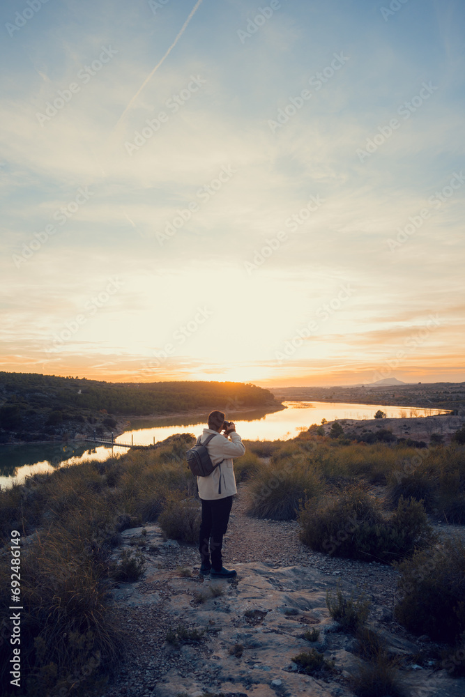 Fototapeta premium Latin photographer with a camera takes photos in a lagoon at sunset