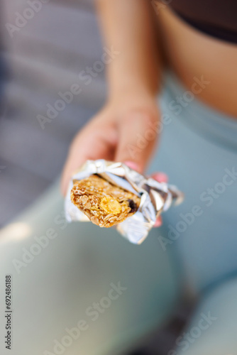 Woman in sportswear holding a protein bar while taking a workout break