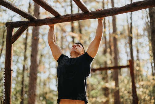 A happy hiker enjoys an active day off surrounded by nature. He explores the wilderness, doing pull ups outdoors with the mountains and forest as his backdrop.