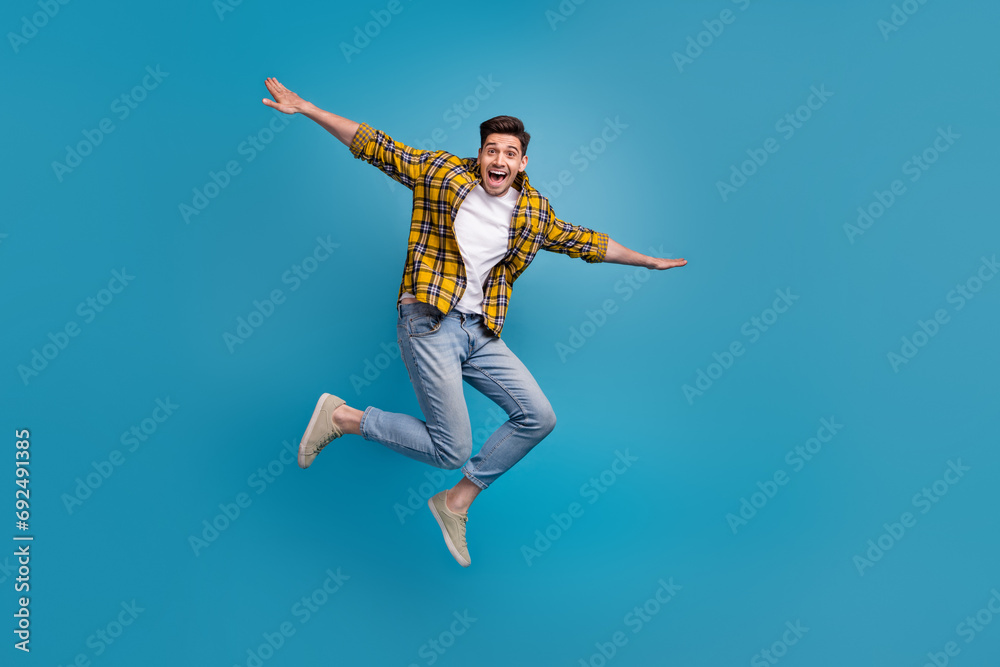 Full body size photo of carefree flying guy enjoying free time spending alone in park wings hands isolated on blue color background Full body size photo of carefree flying guy enjoying free time spending alone in park wings hands isolated on blue color background