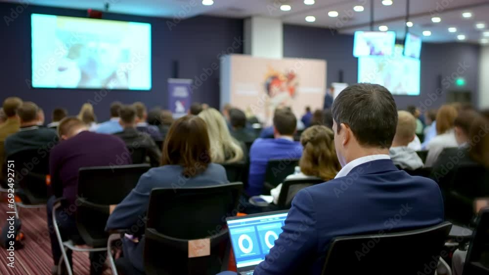 Young man audience at business seminar conference presentation type tablet computer business forum speaker couch. Education auditorium person typing on laptop. People training at economic forum