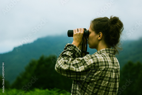 A young adult female looks through binoculars in the foggy mountains