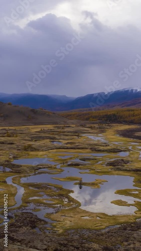 Small Lakes and Clouds Reflection. Larches in Autumn and Mountains. Eshtykel Plateau. The Altai Mountains, Russia. Aerial Hyper Lapse, Time Lapse. Drone Flies Forward. Vertical Video photo