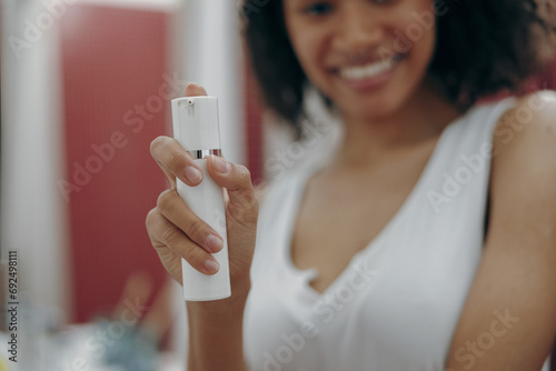 Close up of woman standing at bathroom and holding natural skincare or body care cosmetics bottle
