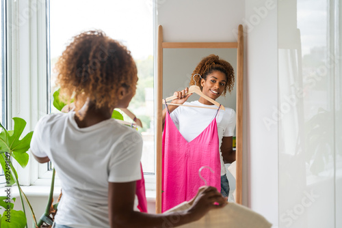 Φωτογραφία Smiling curly woman trying on clothes and looking at her reflection at mirror