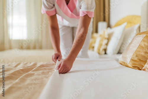 Close up image of hotel maid making bed in a room.