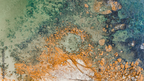 Aerial view from a drone of a natural rock pool in the sea on an Australian beach called Little Bay Beach. green and blue water color along with brown and gray colors of the reefs